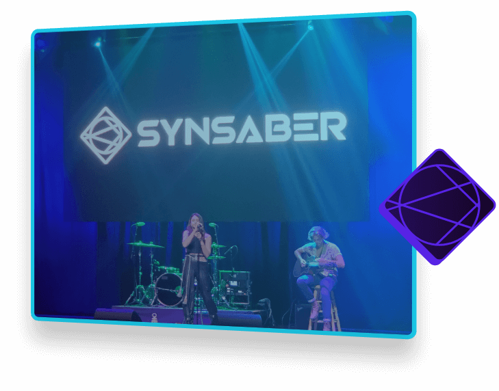 two musicians on stage, with drums and synsaber sign hanging in background